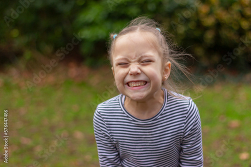 portrait of funny child girl with closed eyes grimacing showing teeth on natural background