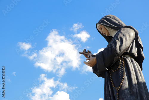 Estátua de Santa Rita de Cássia e céu azul com nuvens ao fundo