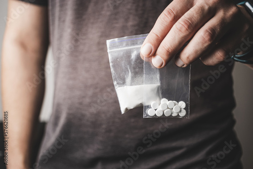 Man's hand holds two transparent plastic packets with cocaine powder and white pills lsd, drug dealer selling drugs. Drug abuse and addiction concept