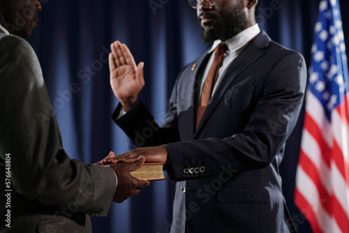 Close-up of young African American man in formalwear giving oath of office with one hand open and the other one on Holy Bible