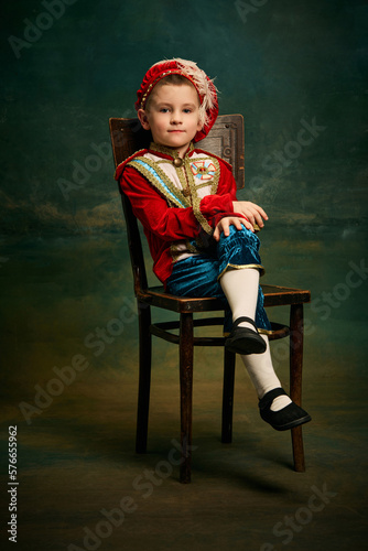 Portrait of cute little boy dressed up as medieval character, little prince and pageboy posing over dark vintage style background, Fashion, emotions, theater art concept