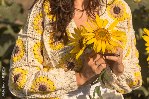closeup of woman in crocheted cardigan holding sunflowers in hand, granny square sunflower, spring summer outfit