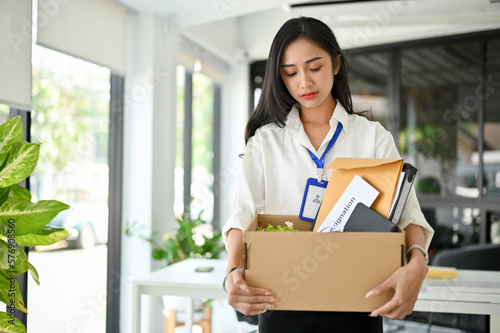 Sad and frustrated Asian female office worker carrying her belonging, quitting a job.