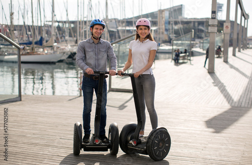 young couple guy and girl are walking on the segway along the board paved promenade in the port of a European city