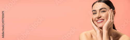 charming young woman with bare shoulders looking at camera while smiling isolated on pink, banner.