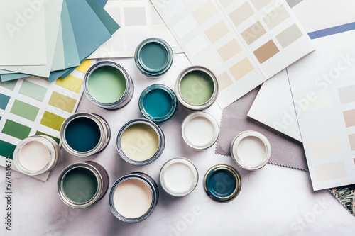 Tiny sample paint cans during house renovation, process of choosing paint for the walls, different green and beige colors, color charts on background