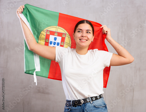 Joyful girl stands with flag of Portugal in her hands. Isolated on gray background