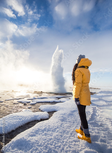 A girl standing in front of Famous Geysir in Iceland in beautiful sunrise light. One of the most famous natural heritage on Iceland.