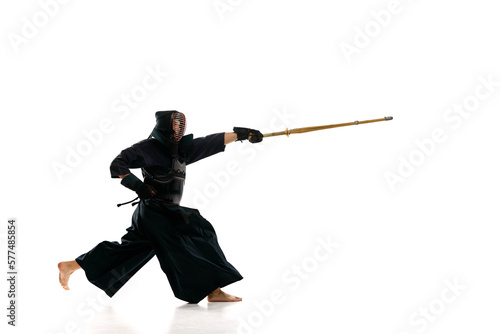 Man, professional kendo athlete in black uniform with sword, shinai training against white studio background. Concept of martial arts, sport, Japanese culture, action and motion, power