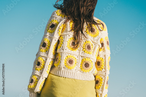 woman from behind with crochet cardigan, granny square sunflower, blue sky background