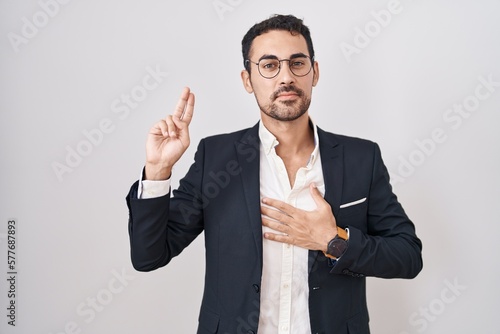 Handsome business hispanic man standing over white background smiling swearing with hand on chest and fingers up, making a loyalty promise oath