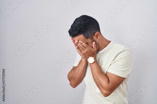 Hispanic man with beard standing over isolated background with sad expression covering face with hands while crying. depression concept.