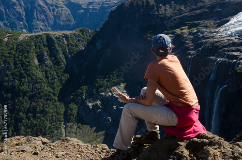 mujer joven con telefono en la mano observando la vista de montañas. en la cordillera de los andes. patagonia argentina cerca de bariloche