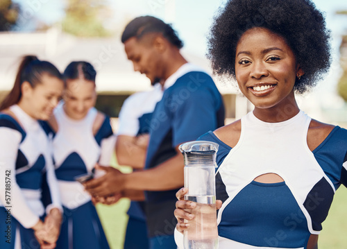 Cheerleader, portrait or black woman drinking water in cheerleading in training or exercise workout. Happy smile, fitness or face of healthy girl athlete with liquid for hydration on field in game
