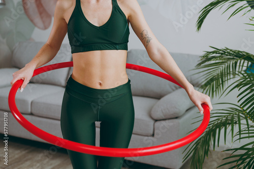 Close up young sporty athletic fitness trainer instructor woman wearing green tracksuit hold using hoola hoop for slim waist training do exercises at home gym indoor. Workout sport motivation concept.