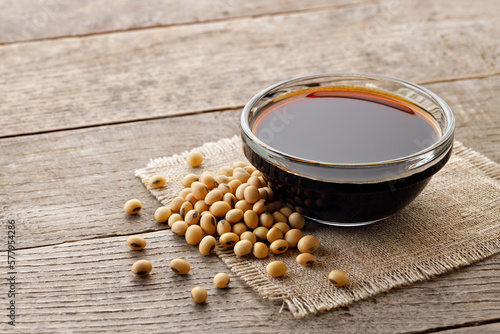 soy sauce in glass bowl with dry soybeans on wooden table