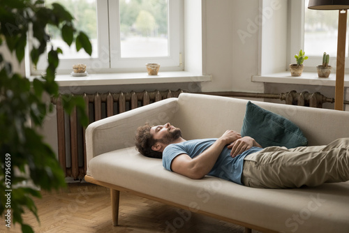 Exhausted peaceful sleepy young woman lying on back on couch with hand on belly, sleeping, resting on sofa at daytime, taking break, pause, feeling fatigue after insomnia