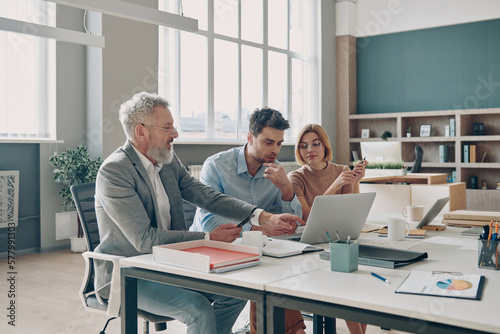 Three confident business people having discussion while working in the office together