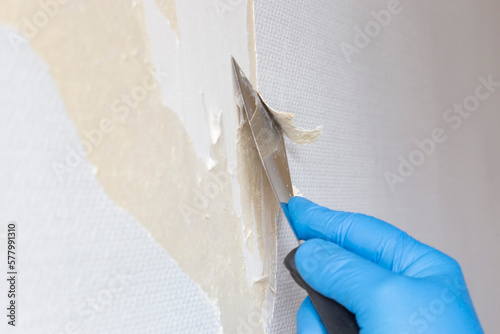 Person stripping wallpaper using a scraper hand tool. Do it yourself concept