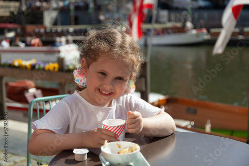 happy little girl sitting in an outdoor cafe. Embankment along the Leie river with medieval houses in the city of Ghent, Belgium.