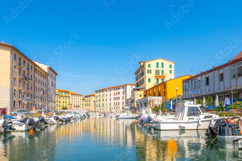 Colorful residential buildings reflect off the water in the boat filled canals at the old port of Livorno, Italy. 