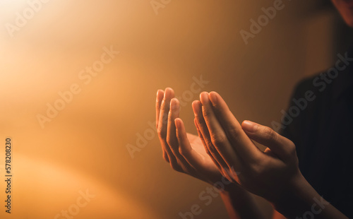 Hand praying on orange light bokeh background.