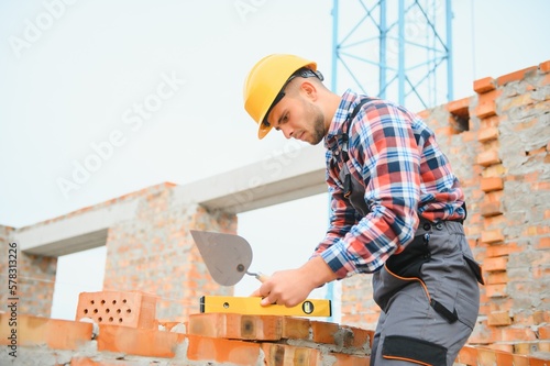 construction mason worker bricklayer installing red brick with trowel putty knife outdoors.