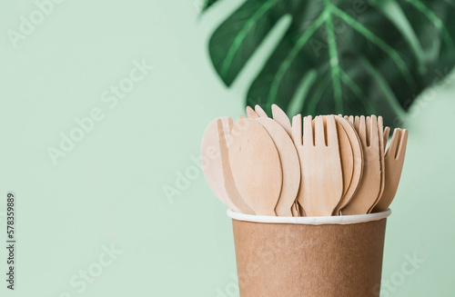 Eco-friendly disposable kitchen utensils in a paper cup on a beige-green background. Wooden forks, spoons and knives. Ecology, the concept of zero waste.