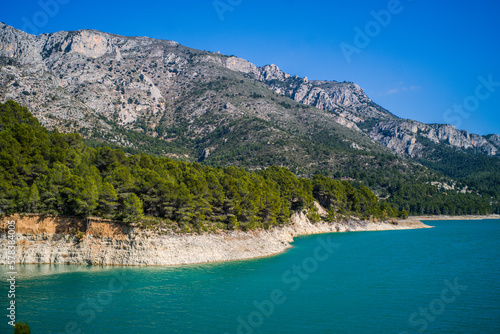 Lake Guadalest, rocky mountains and hills covered with trees. Blue sky