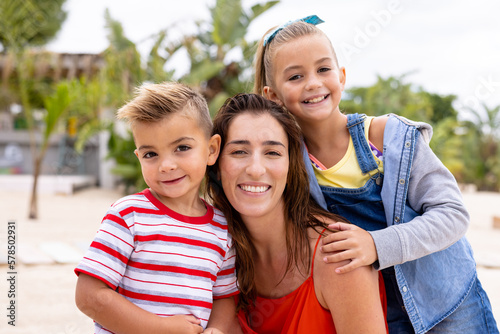 Portrait of happy biracial mother and children embracing and smiling at beach