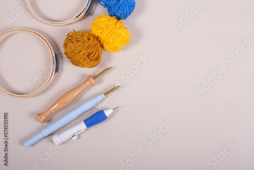 Material para bordar, aguja mágica, bastidor, madejas de lana color azul, amarillo y mostaza para crear punch needle, en superficie lisa neutra bordado colores vivos