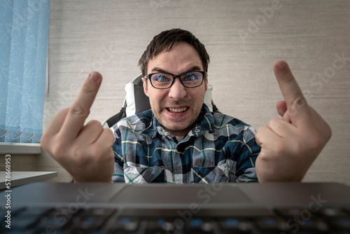 man writes comments while sitting at a laptop and shows his middle finger at a computer screen monitor. insulting and bullying in comments and chats on the Internet. Fuck you sign.
