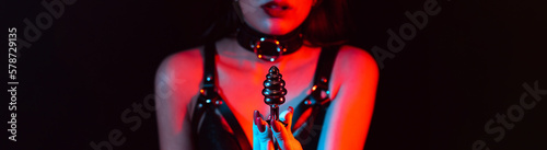 metal butt plug in the hands of a slave girl with a choker and a leather belt. Panoramic wide horizontal photo for banner head cover