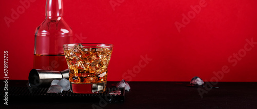 Godfather cocktail with scotch whiskey, almond amaretto liqueur and ice cubes.. Black and red background, steel bar tools, banner