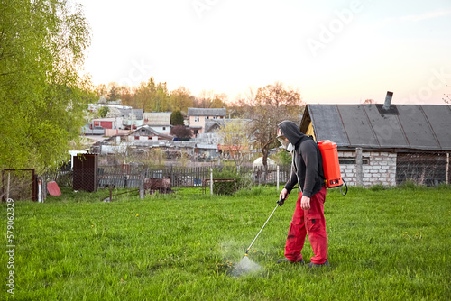 Farmers spraying pesticide on lawn field wearing protective clothing. Insecticide sprayer with a proper protection. Treatment of grass from weeds and dandelion. Copy space. Gardening care season. Man