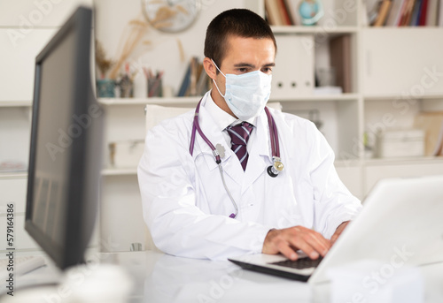 Experienced male therapist wearing surgical mask holding consultation in clinic office