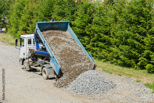 There is a dump truck on a construction site that is dumping gravel on the ground.