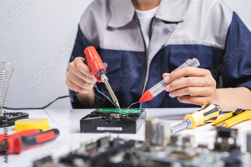 Technician woman repair electronic circuit board with soldering iron and tin wire in her workshop