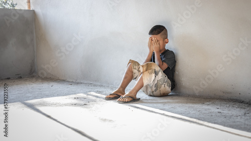 Homeless sad little child sitting alone on floor concrete wall background