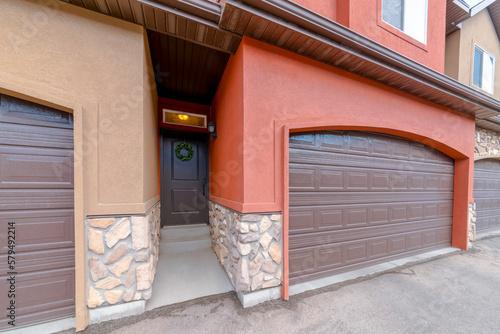 Garages with black front door with wreath entranceway in between the walls. There is a garage with light brown wall on the left and garage with orange wall on the right.