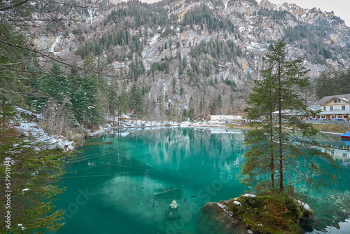 Small lake of turquoise waters in a snowy environment, known as Blausee lake in Switzerland.