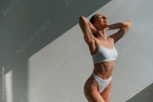 Indoors against the wall, beautiful sunlight. Young caucasian woman with slim body shape is indoors in the studio