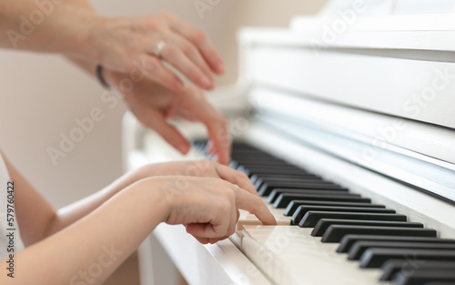 Learning to play the piano, the hands of a child and a teacher on the keys of a white piano