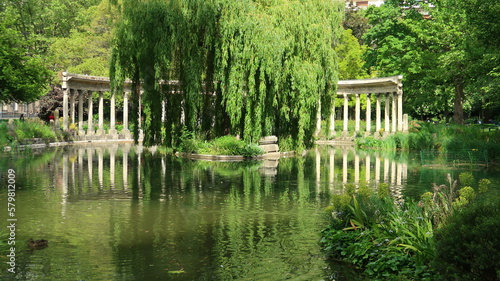 Colonnade corinthienne autour du bassin (naumachie) du parc Monceau à Paris, et son reflet dans l’eau, au milieu de la végétation (France)