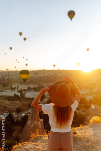 Young woman stands on the mountain with flying air balloons on the background. Famous tourist Turkish region Cappadocia.