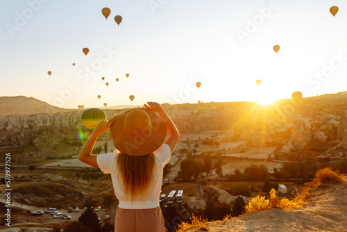 Young woman stands on the mountain with flying air balloons on the background. Famous tourist Turkish region Cappadocia.