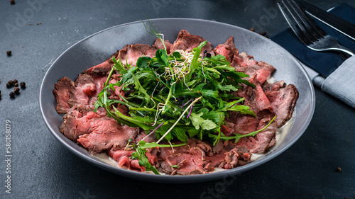 Cold appetizer of beef carpaccio with arugula, microgreens and sauce.