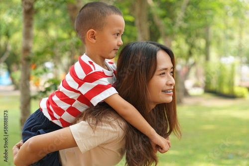 A boy happily rides on his mother's back in the park.