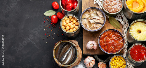 Canned vegetables, beans, fish and fruits in tin cans on black background. Food stocks.