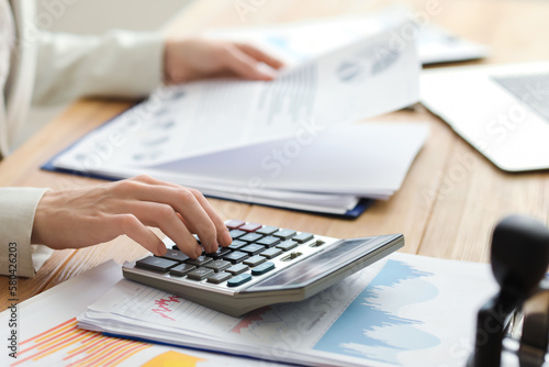 Female accountant working with calculator and documents at table in office, closeup